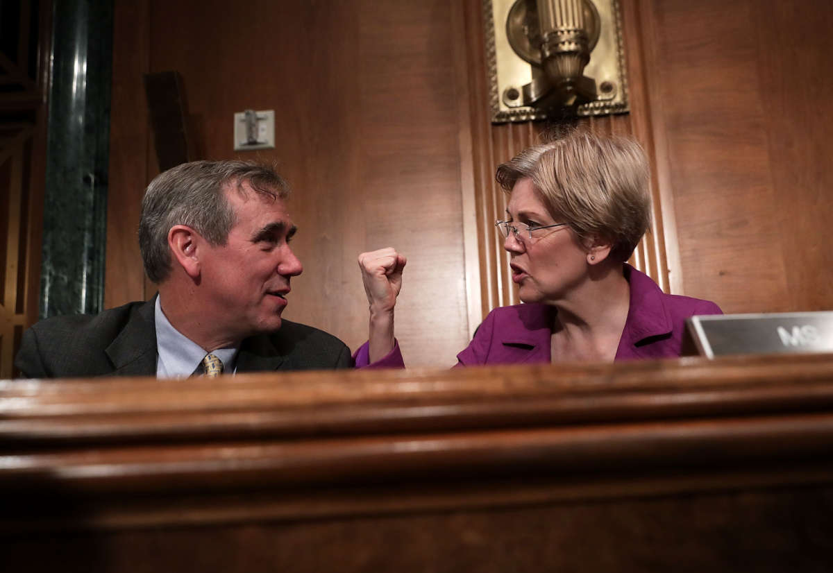 Elizabeth Warren pumps a fist while seated next to Jeff Merkley