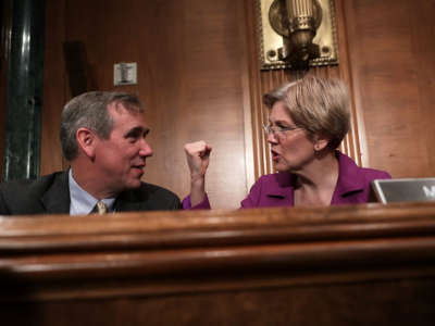 Elizabeth Warren pumps a fist while seated next to Jeff Merkley