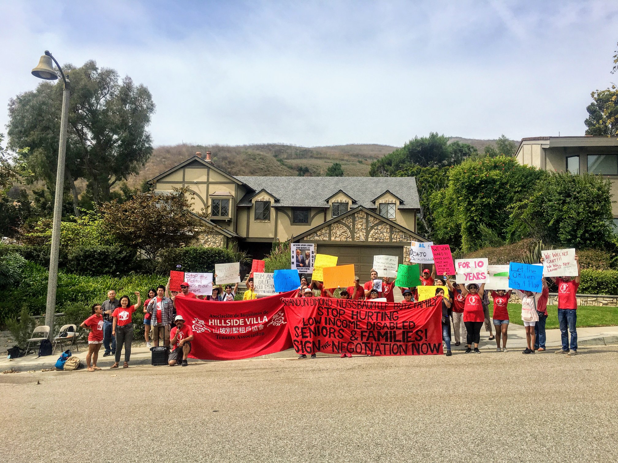 People displaying colorful signs stand in front of a mansion