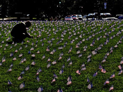 A silhouetted figure kneels in the grass to plant a small u.s. flag in the ground