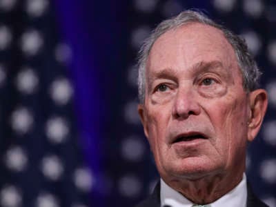 Michael Bloomberg stands in front of a dark blue backdrop