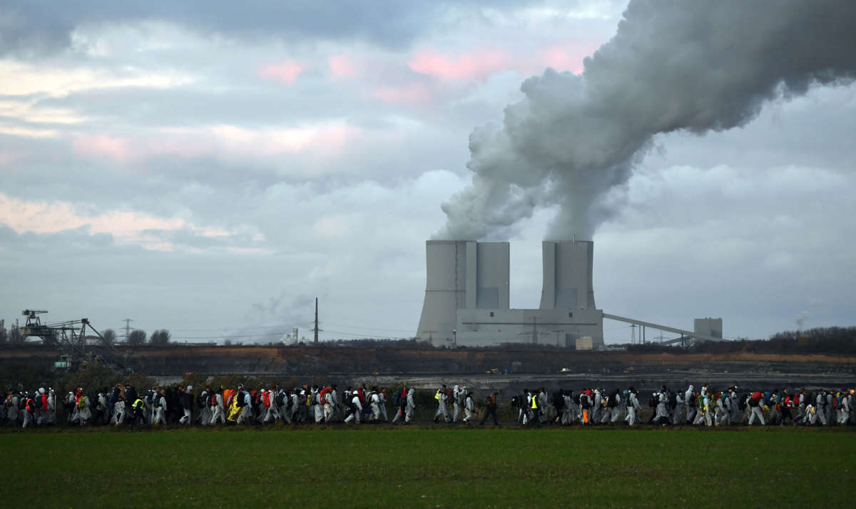 Protesters march as smoke billows from smokestacks in the background