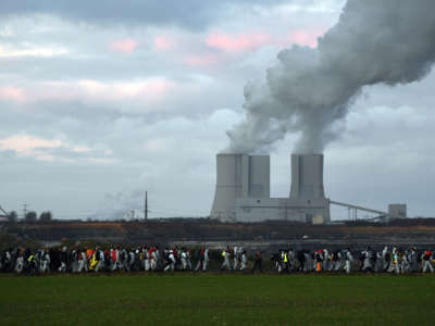 Protesters march as smoke billows from smokestacks in the background