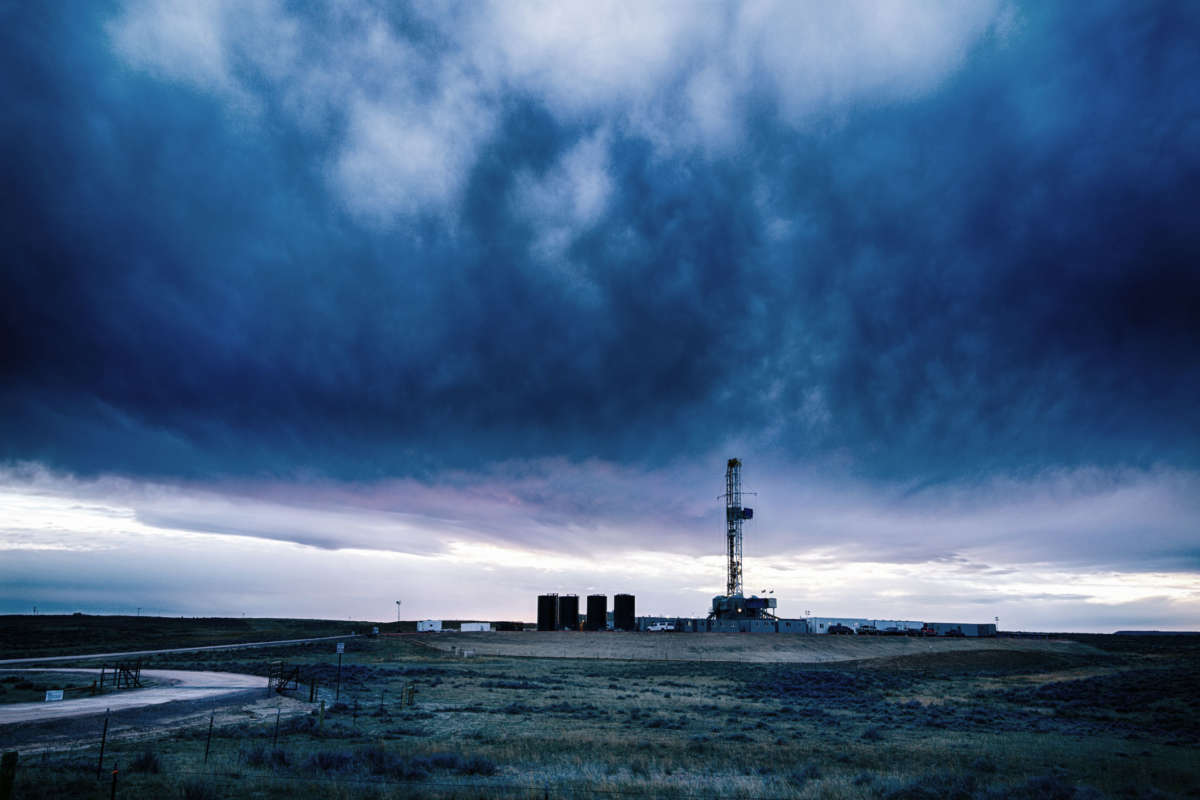 a fracking tower looms in the distance as dark clouds roll over the horizon