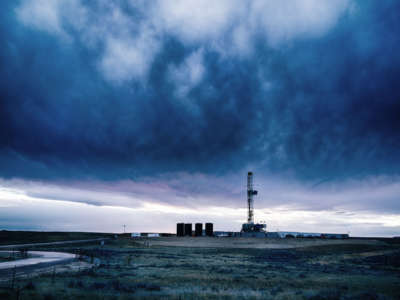 a fracking tower looms in the distance as dark clouds roll over the horizon