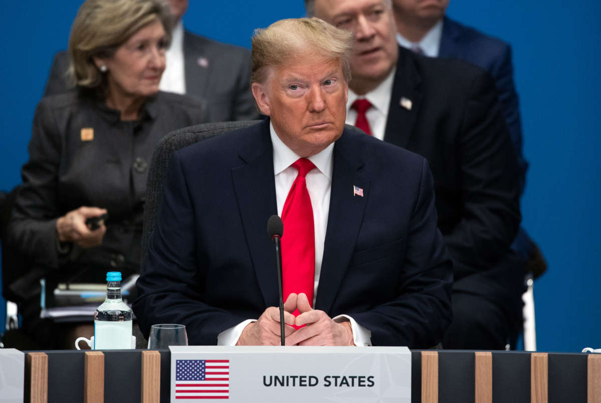 Donald Trump sits at a table designated for the u.s. while other politicians sit behind him