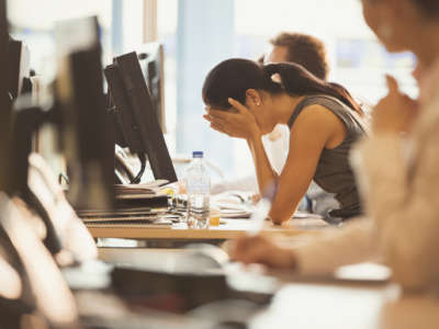 A woman holds her face in her hands while sitting at her desk