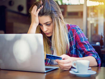 A woman looks stressed at her computer while holding a credit card