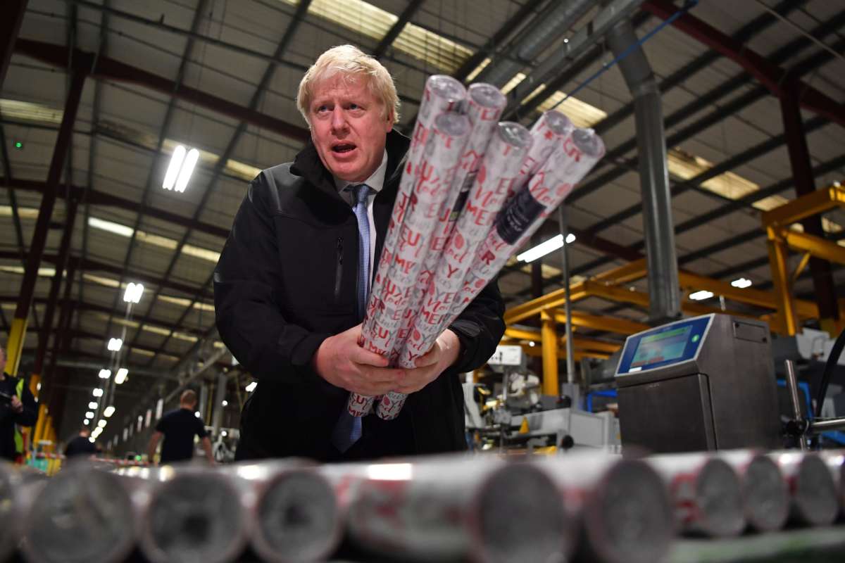 Boris Johnson stands in a factory holding rolls of wrapping paper