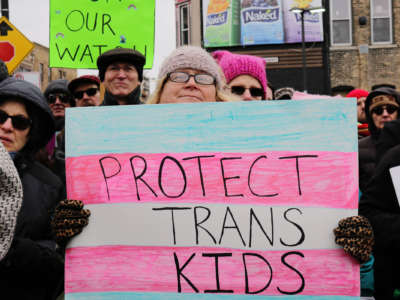 A woman holds a sign reading "PROTECT TRANS KIDS" during a protest
