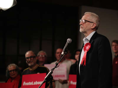 Jeremy Corbyn stands behind a microphone while surrounded by supporters