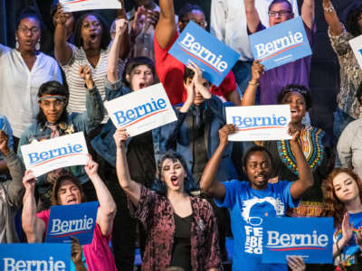 Black and white bernie supporters chant and hold his campaign signs