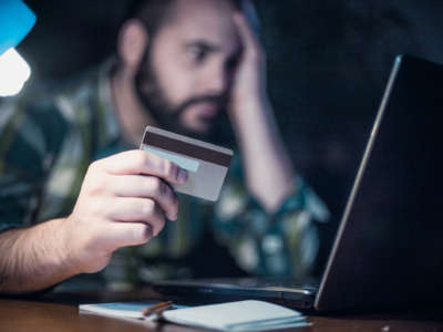 A man looks at his computer screen while holding a credit card