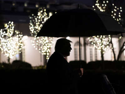 President Trump is seen in silhouette holding an umbrella as he talks to members of the press on the South Lawn of the White House, December 10, 2019.