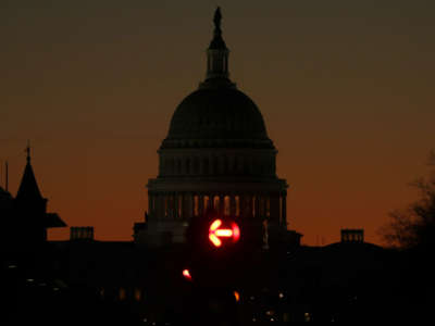 A darkened capitol sits against the setting sun as a red "NO RIGHT TURN" arrow is illuminated in the foreground