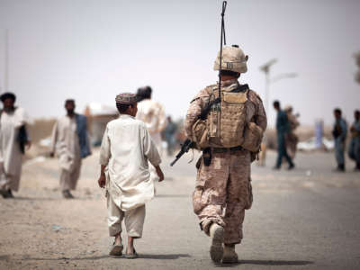 An Afghan boy walks alongside a U.S. Marine on a security patrol in Helmand Province, Afghanistan, on April 17, 2012.