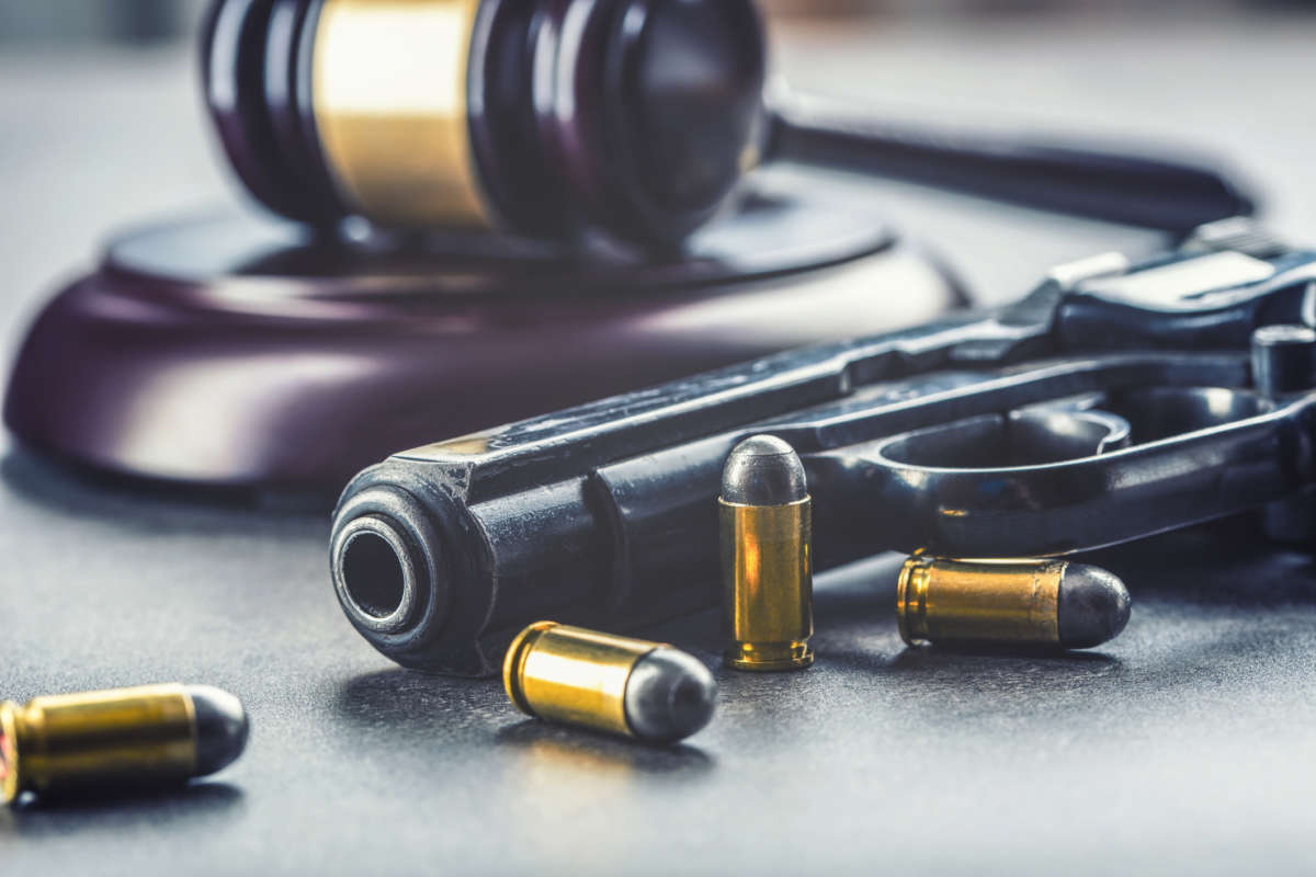 A gun and bullets lie on a table in front of a gavel