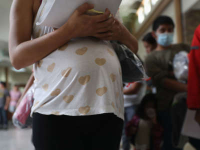 A pregnant Honduran immigrant stands in line with fellow immigrants for a bus to a U.S. destination on August 15, 2016, from McAllen, Texas.
