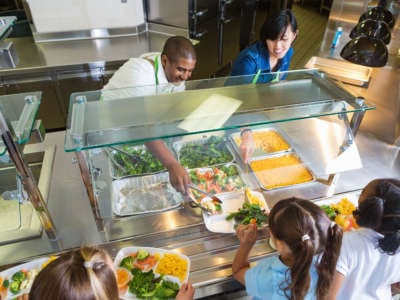Cafeteria worker serving trays of healthy food to children