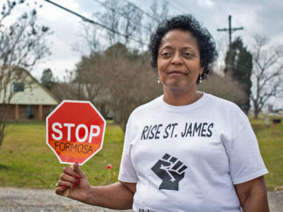 A woman holds a small stop sign with "STOP FERMOSA" written on it