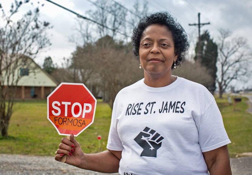 A woman holds a small stop sign with "STOP FERMOSA" written on it