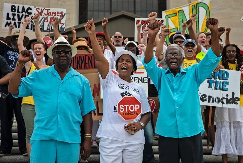 people raise their fists and signs during a protest