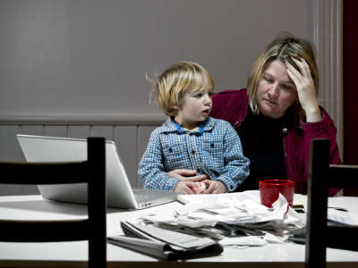 A woman sits with her child on her lap while looking despondently at bills