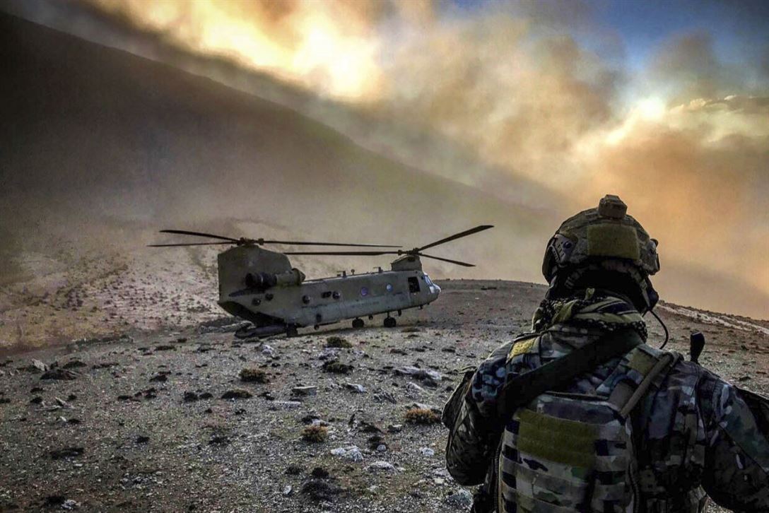A soldier in fatigues looks at a helicopter on the dusty side of a mountain