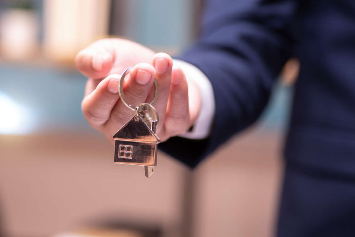A man offers a key with a house-shaped keychain attached