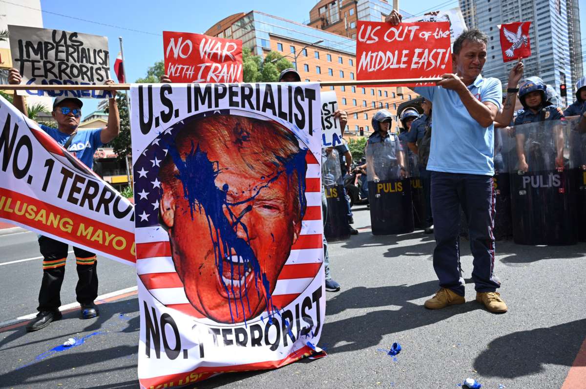 Protesters display a paint-splattered sign showing donald trump's face with the caption "U.S. IMPERIALIST; NO. 1 TERRORIST"