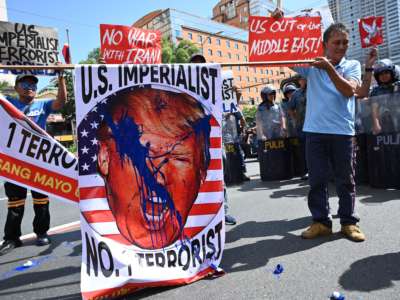 Protesters display a paint-splattered sign showing donald trump's face with the caption "U.S. IMPERIALIST; NO. 1 TERRORIST"