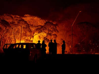 Residents look on as flames burn through bush on January 4, 2020, in Lake Tabourie, Australia.