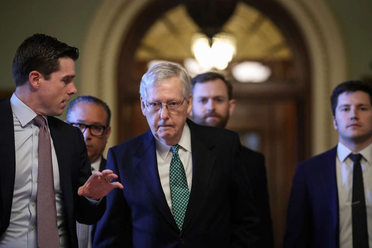 Mitch Mcconnell walks down a hallway flanked by other white men