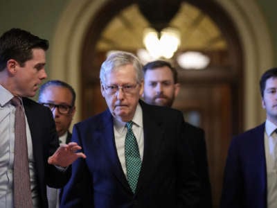 Mitch Mcconnell walks down a hallway flanked by other white men
