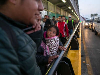 A little girl waits in a long line with other migrants from Central and South America