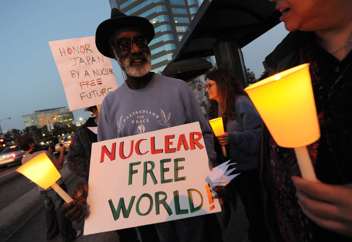 A man holds a sign reading "NUCLEAR FREE WORLD!" during a candlelight vigil