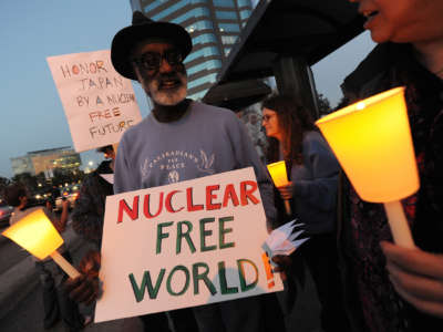 A man holds a sign reading "NUCLEAR FREE WORLD!" during a candlelight vigil