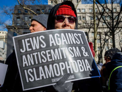 A woman holds a sign reading "JEWS AGAINST ANTISEMITISM AND ISLAMOPHOBIA" during a rally