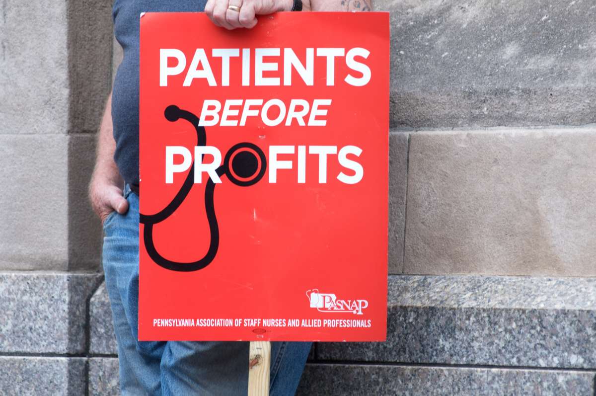 A person displays a sign reading "PATIENTS BEFORE PROFITS"