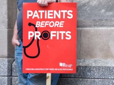 A person displays a sign reading "PATIENTS BEFORE PROFITS"