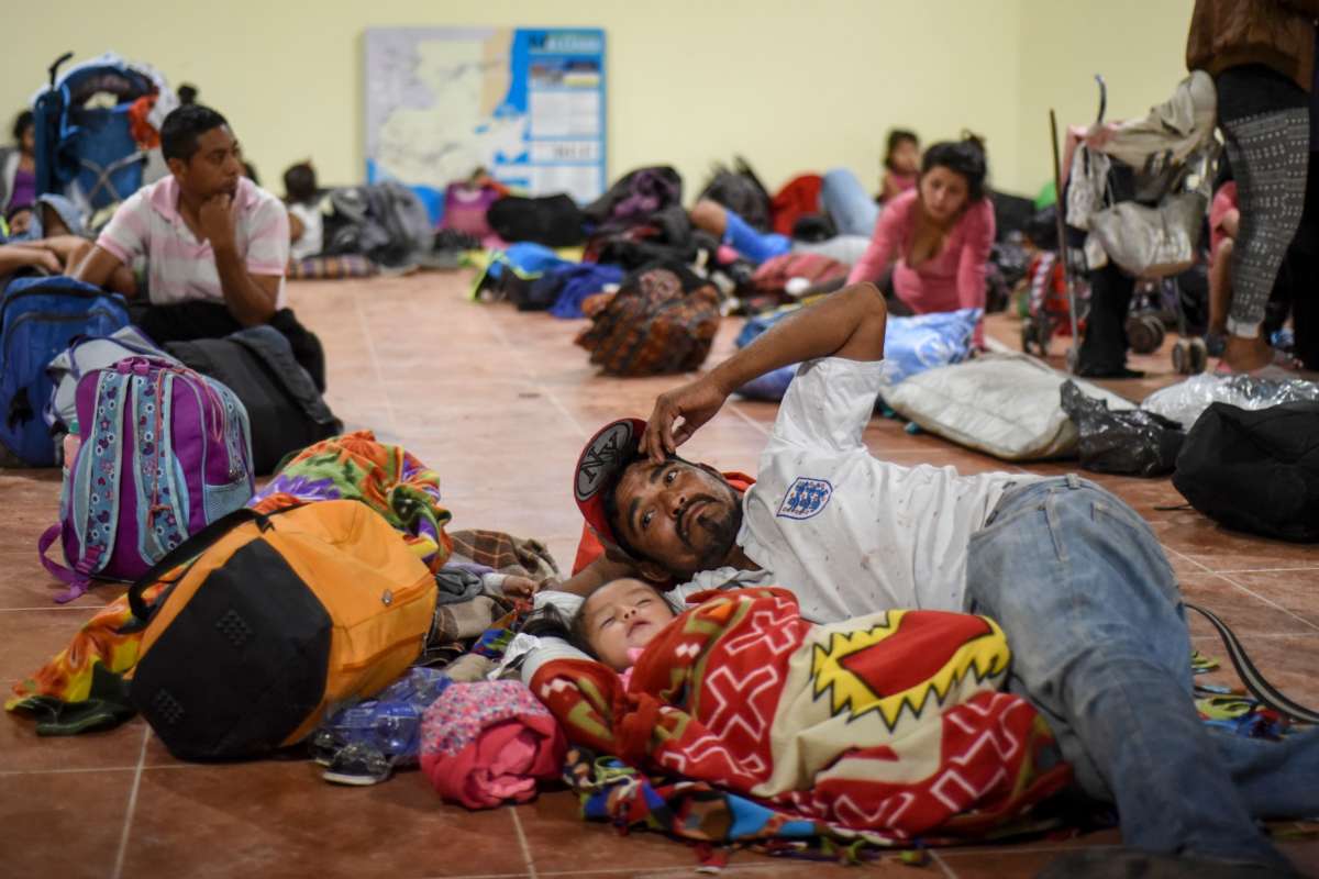 A father lays on the ground with his daughter alongside many other migrants