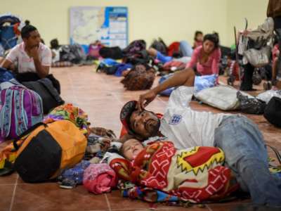 A father lays on the ground with his daughter alongside many other migrants