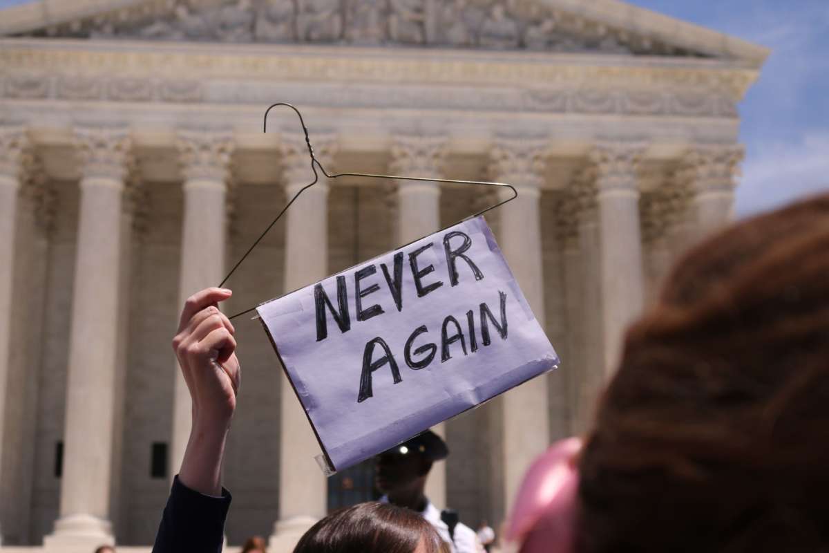 A protester holds a sign affixed to a wire hanger that reads "NEVER AGAIN"