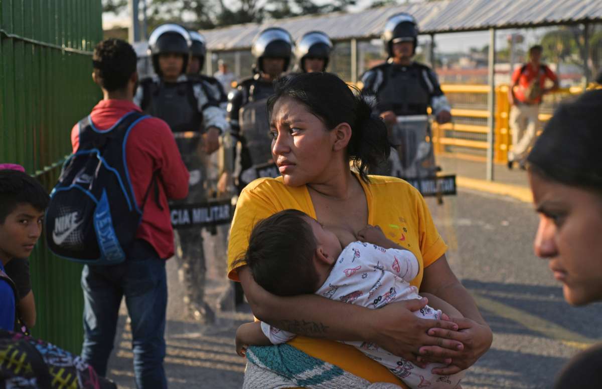 A woman holds her baby while police stand behind her