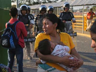 A woman holds her baby while police stand behind her