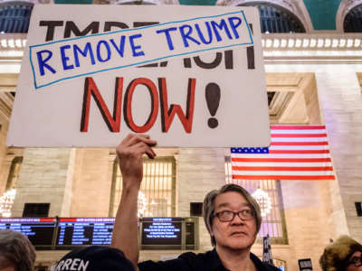A protester holds a sign reading "REMOVE TRUMP NOW!"