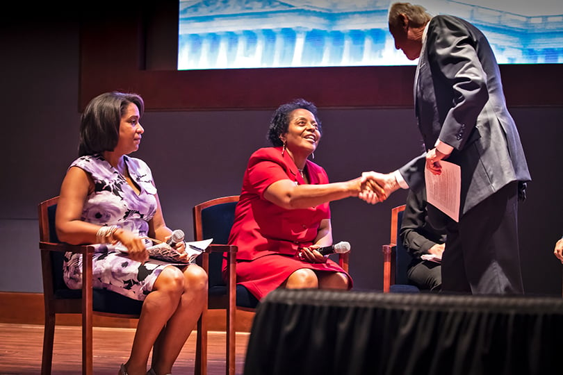 Sharon Lavinge shakes a man's hand while seated in a chair onstage