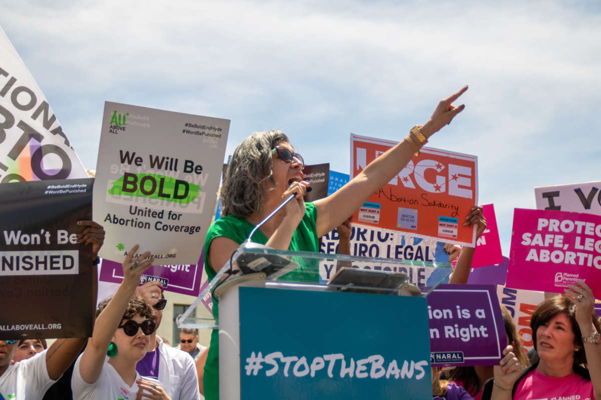 A woman speaks into a microphone as pro-choice protesters display signs behind her