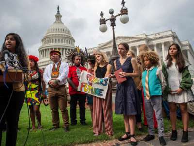 Young climate activists watch another youth speak at a podium