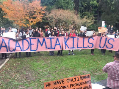 A large group of people hold a sign reading "academia is killing us" outside humanities buildings at University of California Santa Cruz, December 12, 2019.